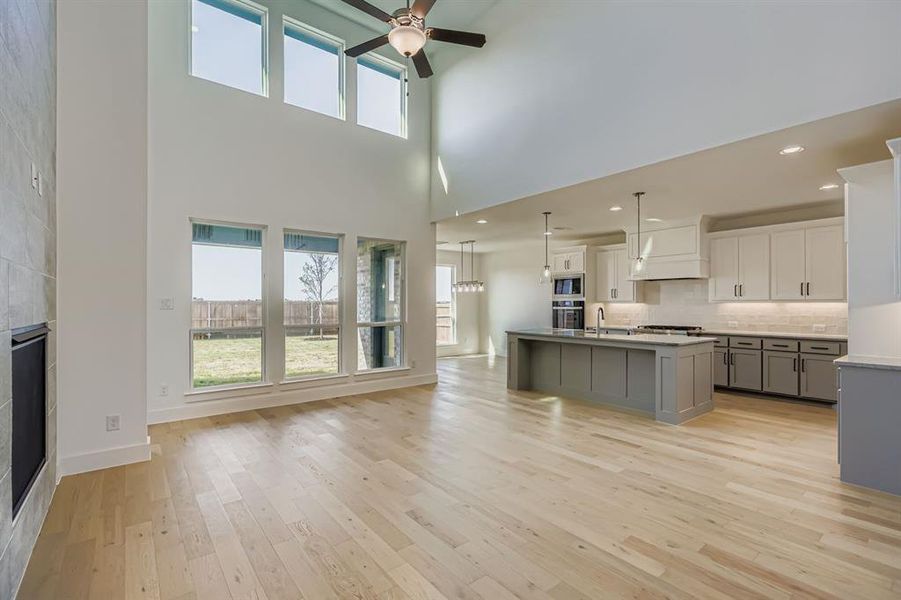 Kitchen featuring gray cabinetry, backsplash, plenty of natural light, light wood-style flooring, and a towering ceiling Kitchen featuring gray cabinetry, backsplash, plenty of natural light, light wood-style flooring, and a towering ceiling