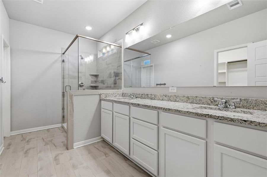 Bathroom featuring double vanity, a walk in closet, a stall shower, light wood-style floors, and recessed lighting