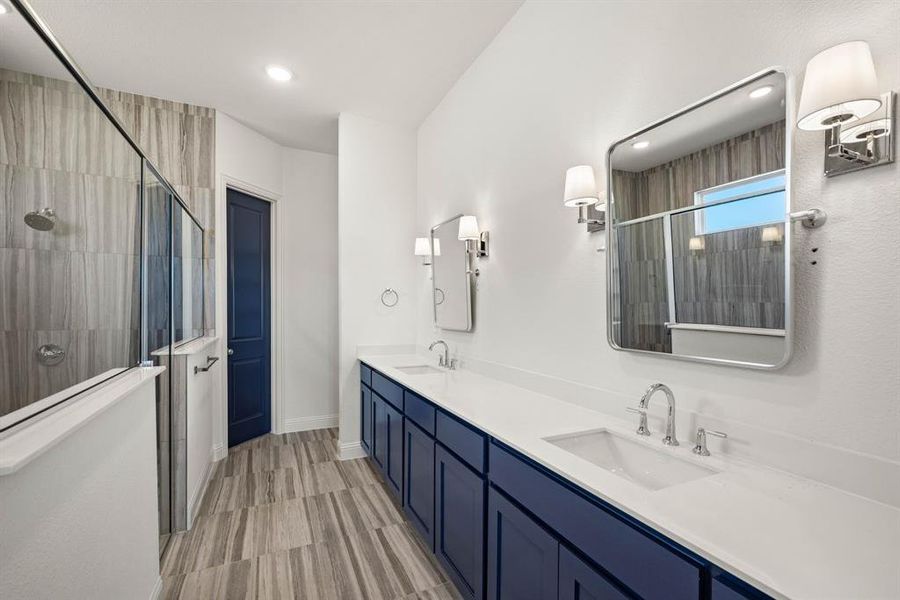 Bathroom featuring double vanity, tiled shower, a sink, and baseboards