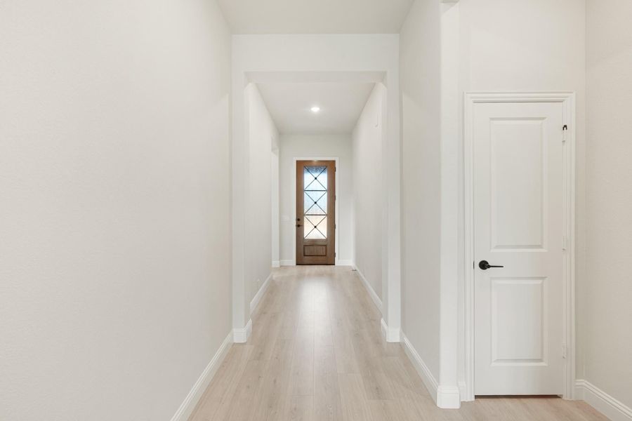 Bright hallway with light wood floors, white walls, and wood front door with glass panels at the end