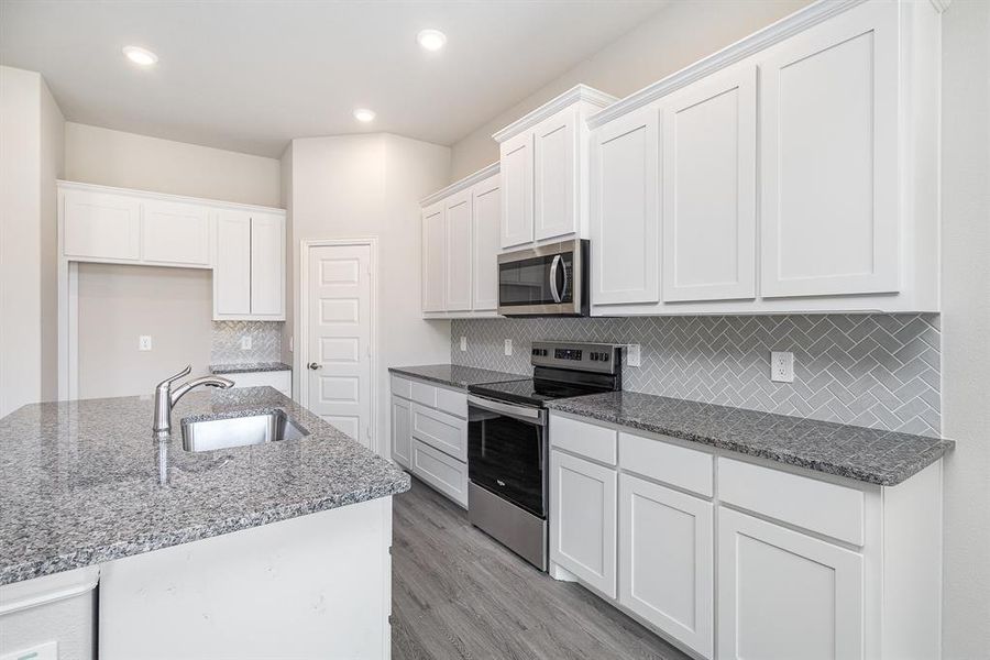 Kitchen with dark stone counters, white cabinets, sink, appliances with stainless steel finishes, and light hardwood / wood-style floors