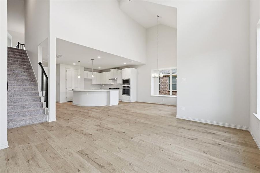 Unfurnished living room featuring stairway, light wood-style floors, a chandelier, and a high ceiling Unfurnished living room featuring stairway, light wood-style floors, a chandelier, and a high ceiling