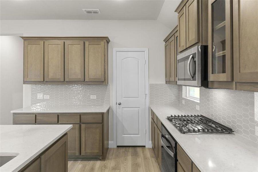 Kitchen with light stone countertops, light hardwood / wood-style flooring, tasteful backsplash, and appliances with stainless steel finishes