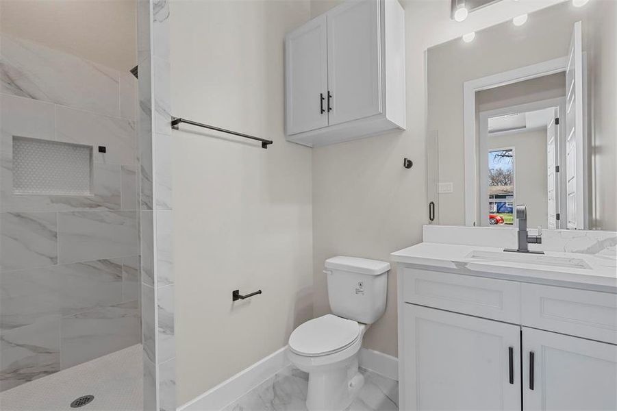 Bathroom featuring a tile shower, vanity, and toilet