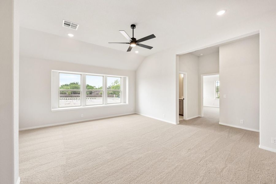 Spacious empty bedroom with vaulted ceiling, ceiling fan, carpet flooring, and large windows