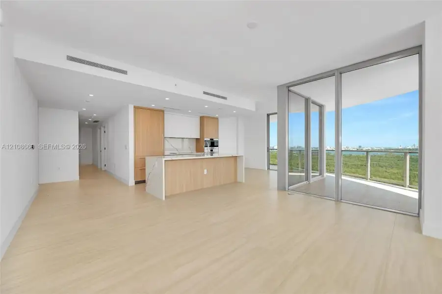 Open-concept interior featuring wood-finish flooring, kitchen island with stone-surface countertop, floor-to-ceiling glass sliding doors, and built-in stainless steel wall oven