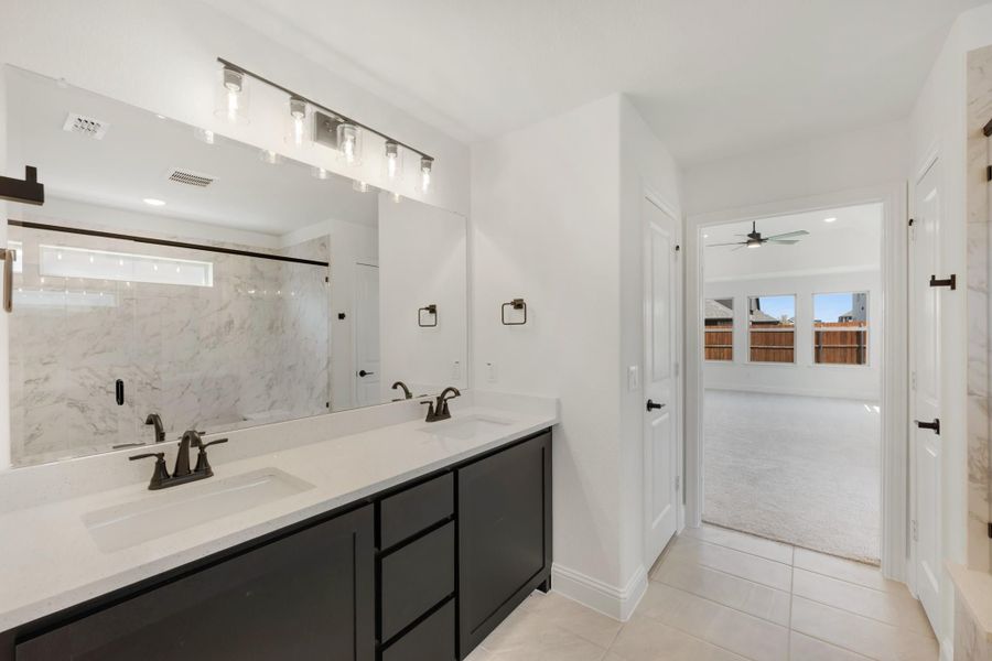 Bathroom with double vanity, dark cabinets, white countertops, and marble tile shower surround