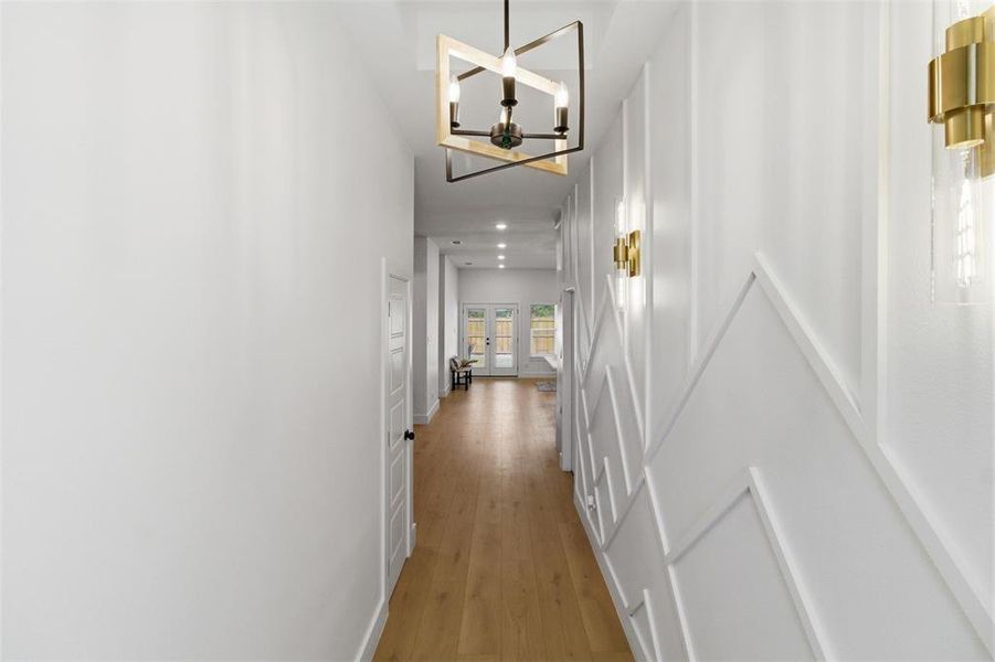 Long corridor featuring light wood-finish flooring, white walls, and a contemporary linear light fixture