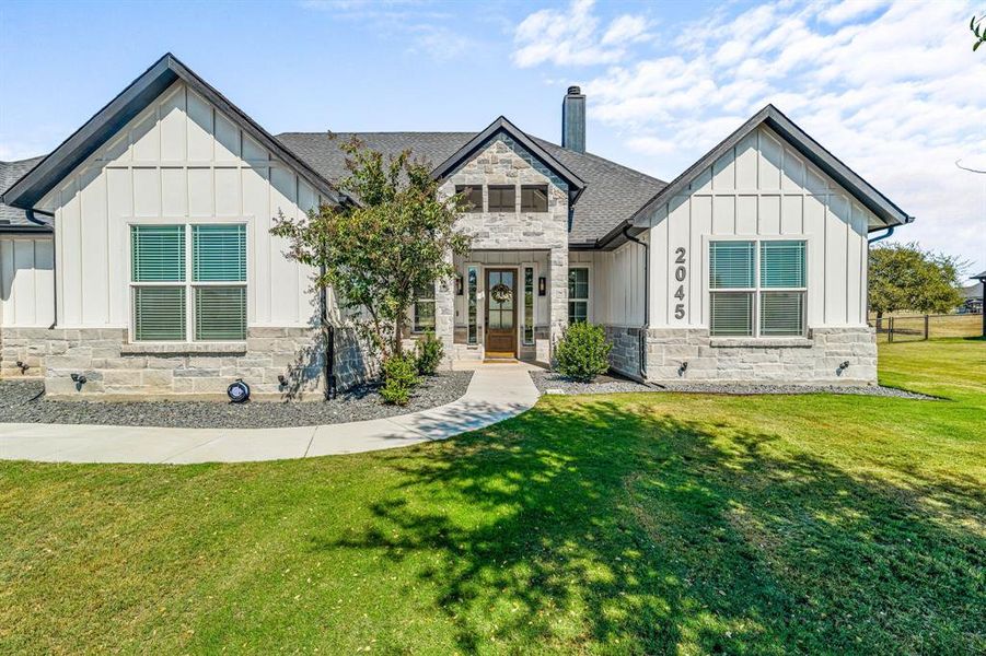 Modern inspired farmhouse with board and batten siding, stone siding, a front lawn, and a chimney