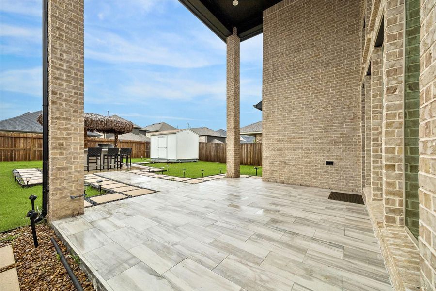 The covered patio extends the living space outdoors with soaring brick columns, stylish tile, and a beautiful view of the backyard retreat.