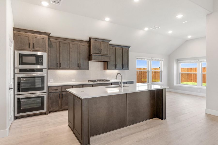 Kitchen with dark wood cabinets, center island with sink, double wall oven, and light hardwood floors Kitchen with dark wood cabinets, center island with sink, double wall oven, and light hardwood floors