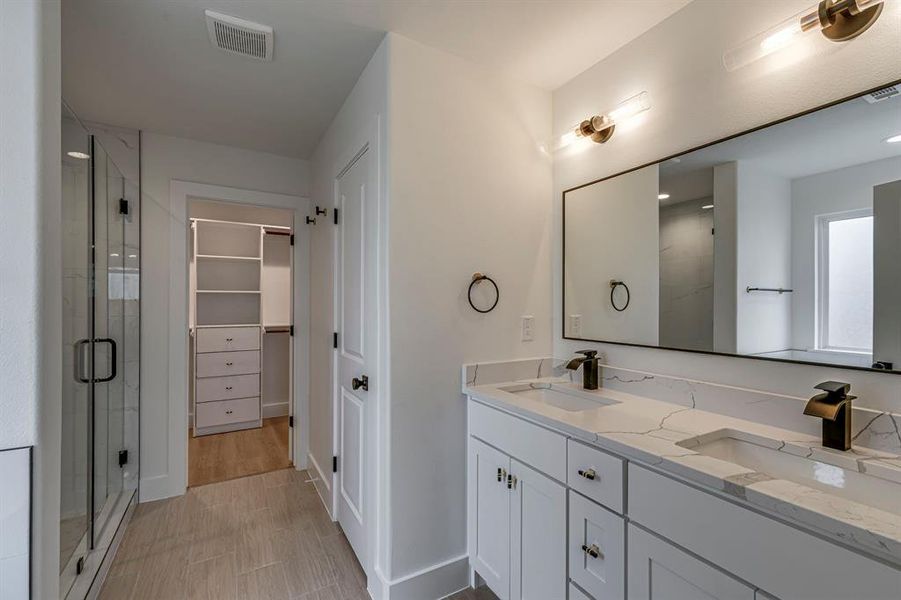 Bathroom featuring a stall shower, a spacious closet, visible vents, and a sink