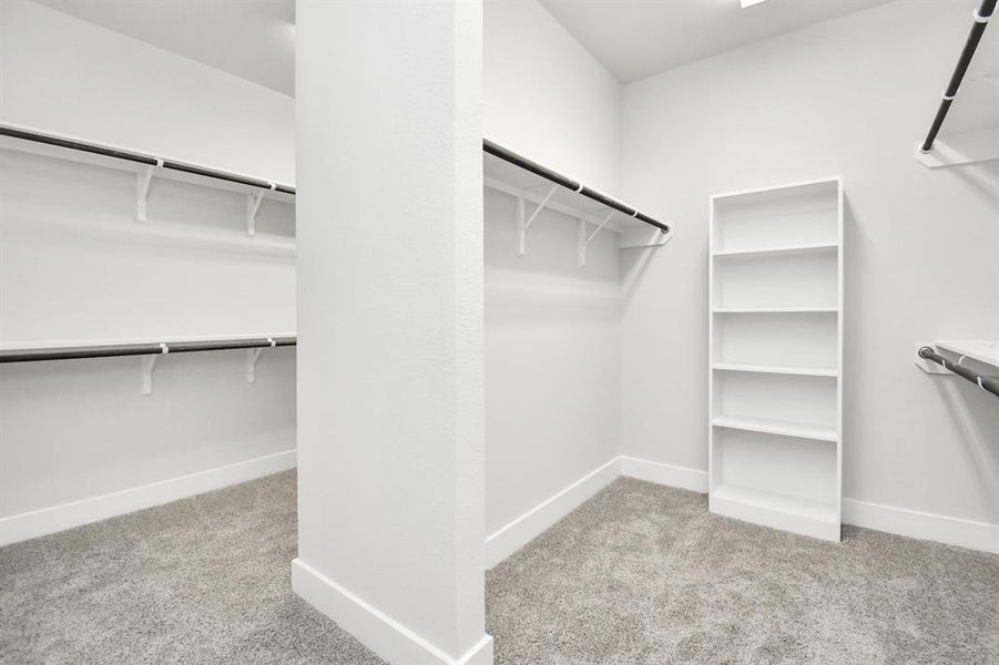 Step into a walk-in closet that defines luxury and functionality. This generously sized space boasts built-in shelving, providing ample room for organization. With high ceilings and recessed lighting, the ambiance is both bright and welcoming. Plush carpeting underfoot enhances the comfort, while warm paint tones add a touch of coziness. Sample photo of completed home. Actual colors and selections will vary.