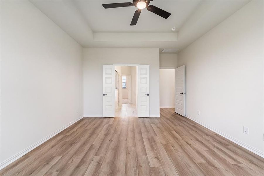 Unfurnished bedroom featuring light wood-style floors, a tray ceiling, and a ceiling fan