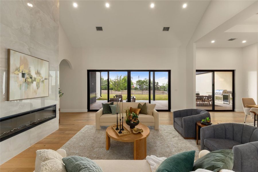 Living room with light wood-style flooring, vaulted ceiling, recessed lighting, and a glass covered fireplace