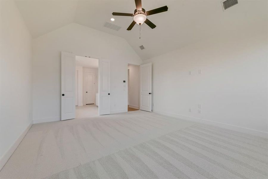 Unfurnished bedroom featuring light colored carpet, vaulted ceiling, and a ceiling fan