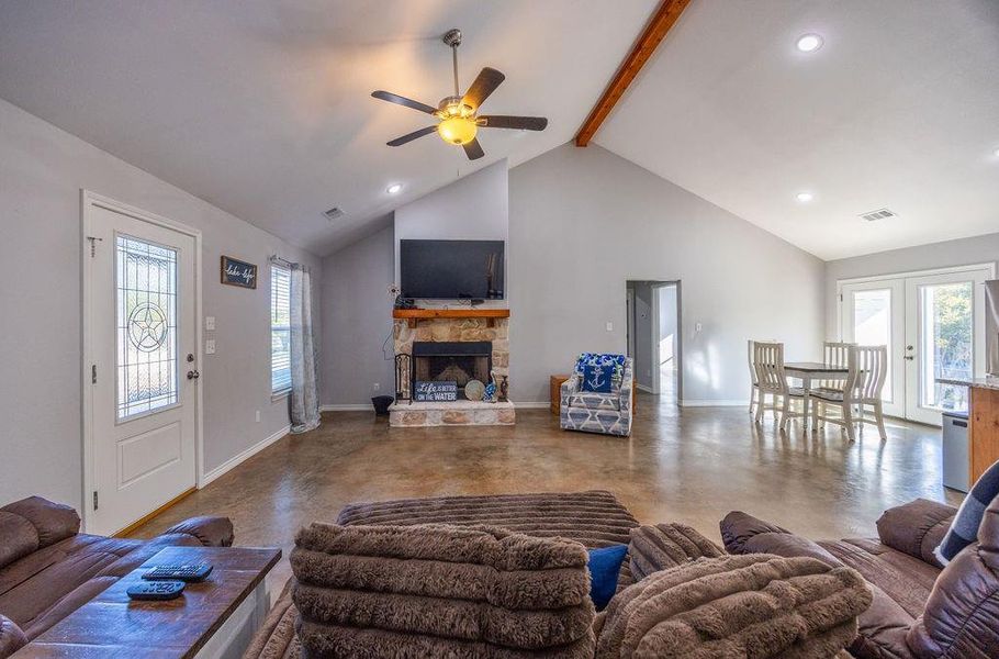 Living area featuring beamed ceiling, concrete floors, a fireplace, healthy amount of natural light, and high vaulted ceiling