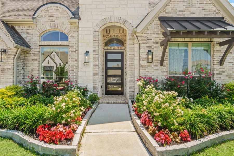 This charming home features a welcoming arched entrance with a modern glass paneled door, beautiful brickwork, and a lush, colorful landscaping. Ideal for buyers seeking an elegant one story.