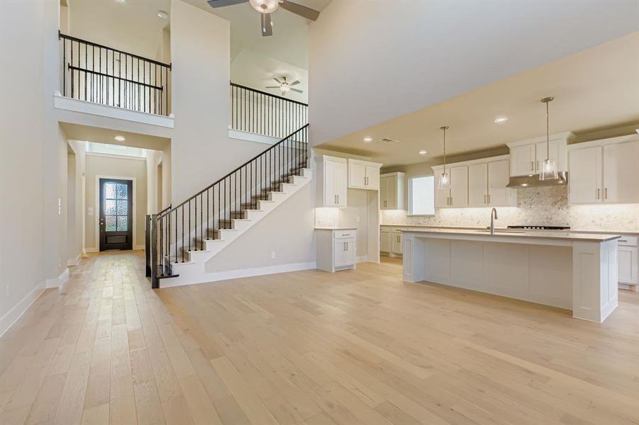 Kitchen featuring light wood-style flooring, backsplash, white cabinets, an island with sink, and hanging light fixtures