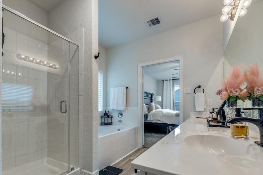 Modern bathroom with a glass-enclosed shower, a bathtub, and a double vanity. The space is bright with neutral colors and features a doorway leading to a cozy bedroom.