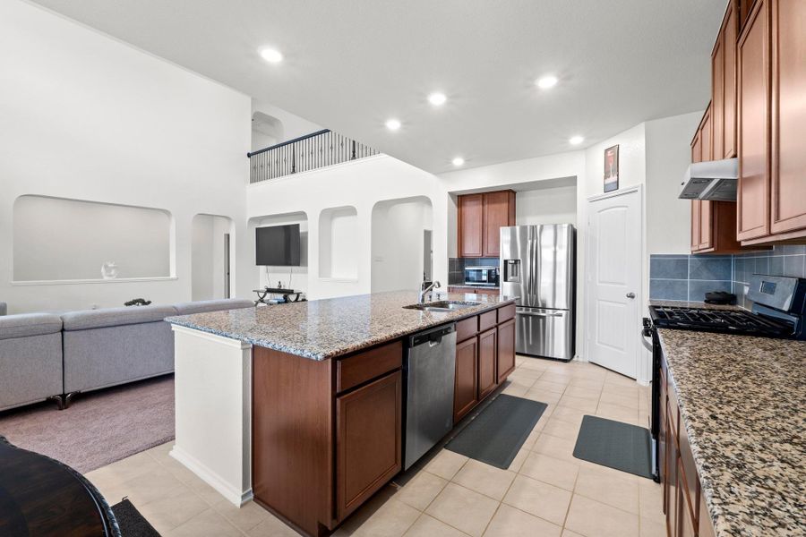 Spacious kitchen featuring an expansive center island with granite countertops, stainless steel appliances, wood cabinetry, and tile flooring