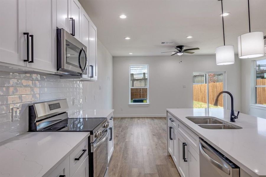Kitchen with stainless steel appliances, light stone countertops, backsplash, hanging light fixtures, and recessed lighting Kitchen with stainless steel appliances, light stone countertops, backsplash, hanging light fixtures, and recessed lighting