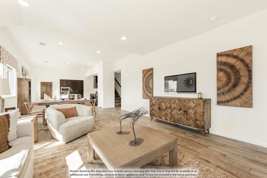 Open living room with wood floors, neutral furniture, and kitchen visible in background