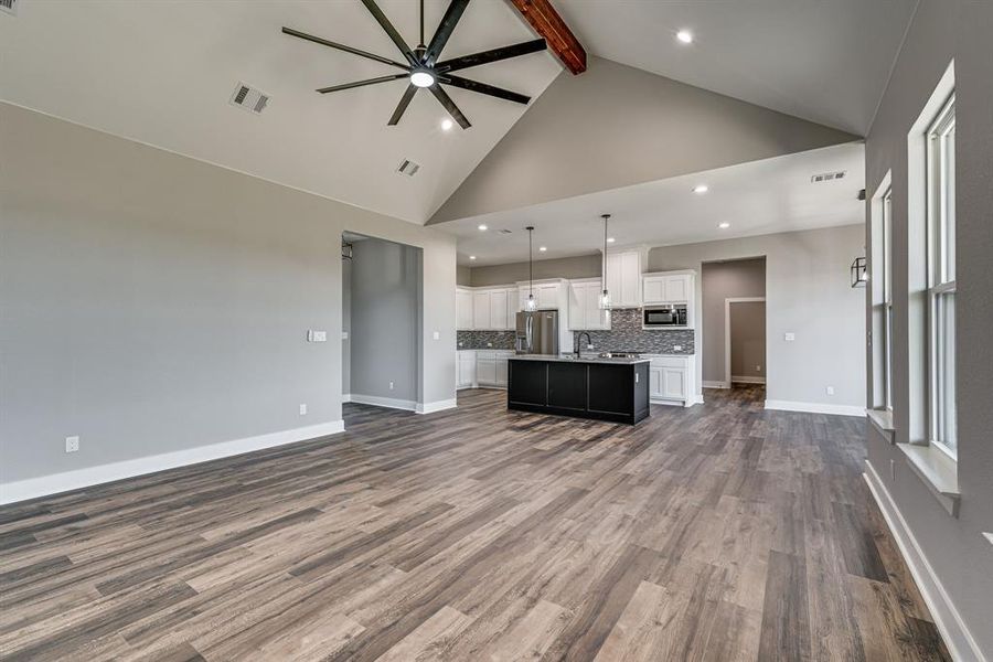 Unfurnished living room with ceiling fan, beam ceiling, dark hardwood / wood-style flooring, sink, and high vaulted ceiling