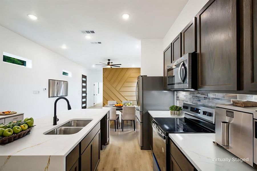 Kitchen with dark wood finish cabinets, stainless steel appliances, light stone counters, light wood-type flooring, and recessed lighting