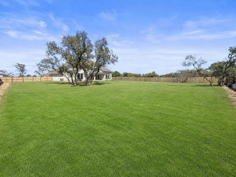 An expansive green yard extends toward a charming single-story home nestled amongst mature trees. An expansive green yard extends toward a charming single-story home nestled amongst mature trees.