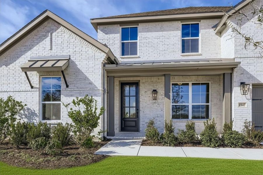 Property entrance with brick siding, a porch, a lawn, and a standing seam roof