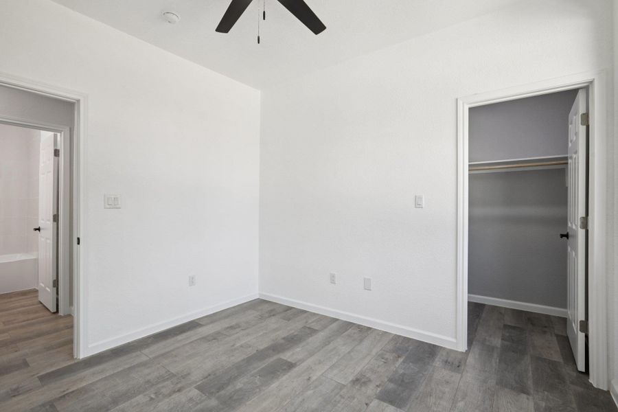 Bedroom 2 with a spacious closet, ceiling fan, and light wood-type laminate flooring