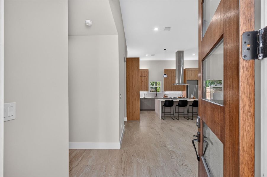 Step into a modern, open-concept kitchen featuring sleek wood cabinetry, a central island with bar seating, and stainless steel appliances, all illuminated by stylish pendant lighting.