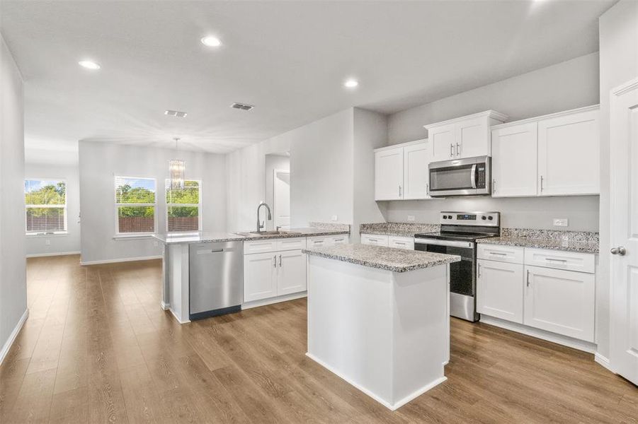 Kitchen with light wood-type flooring, white cabinets, stainless steel appliances, and a kitchen island with sink