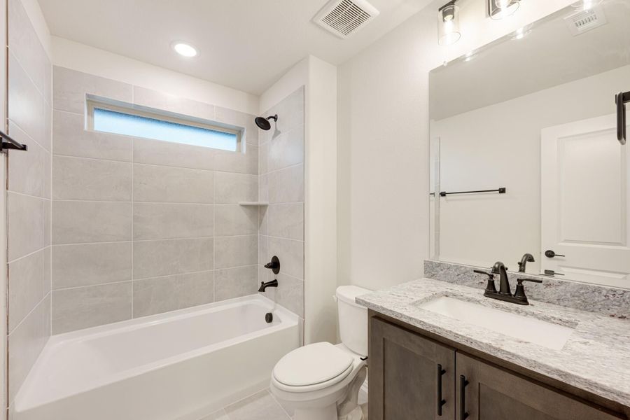 Bathroom with tiled tub-shower combo, granite vanity, dark fixtures, and large mirror Bathroom with tiled tub-shower combo, granite vanity, dark fixtures, and large mirror