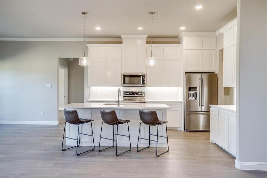 Kitchen with sink, ornamental molding, an island with sink, and appliances with stainless steel finishes