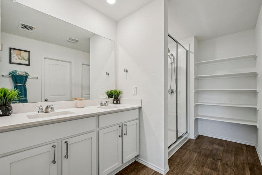 Full bath with a stall shower, double vanity, and dark wood-style floors