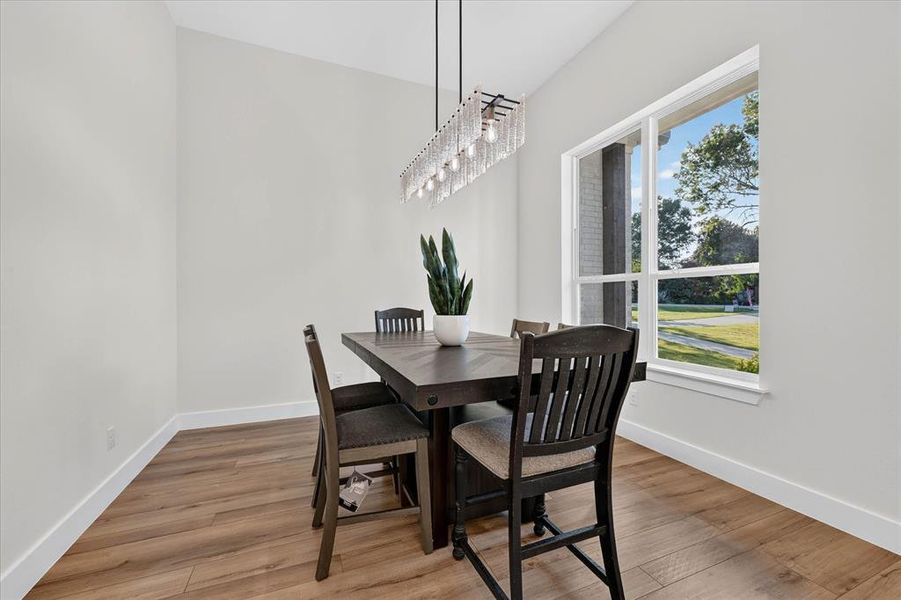 Dining area featuring wood-finish flooring, vaulted ceiling, and a linear chandelier with glass accents Dining area featuring wood-finish flooring, vaulted ceiling, and a linear chandelier with glass accents