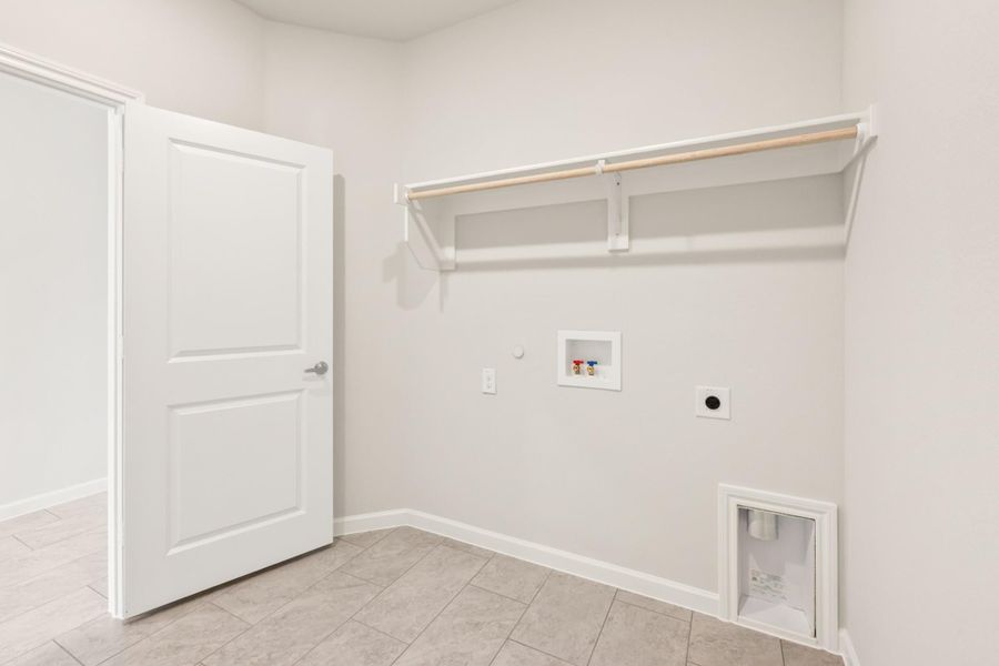 Laundry room with wall-mounted shelf, washer hookups, dryer outlet, pet door, and tile floor Laundry room with wall-mounted shelf, washer hookups, dryer outlet, pet door, and tile floor