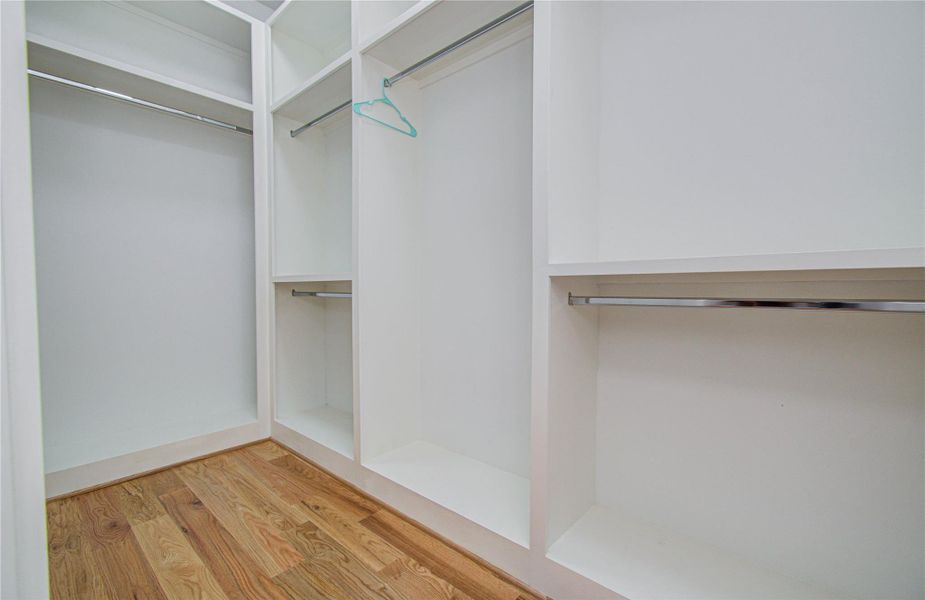 The primary bedroom features a spacious walk-in closet with white shelving and multiple hanging rods, set against a warm wooden floor. Perfect for ample clothing storage and organization.