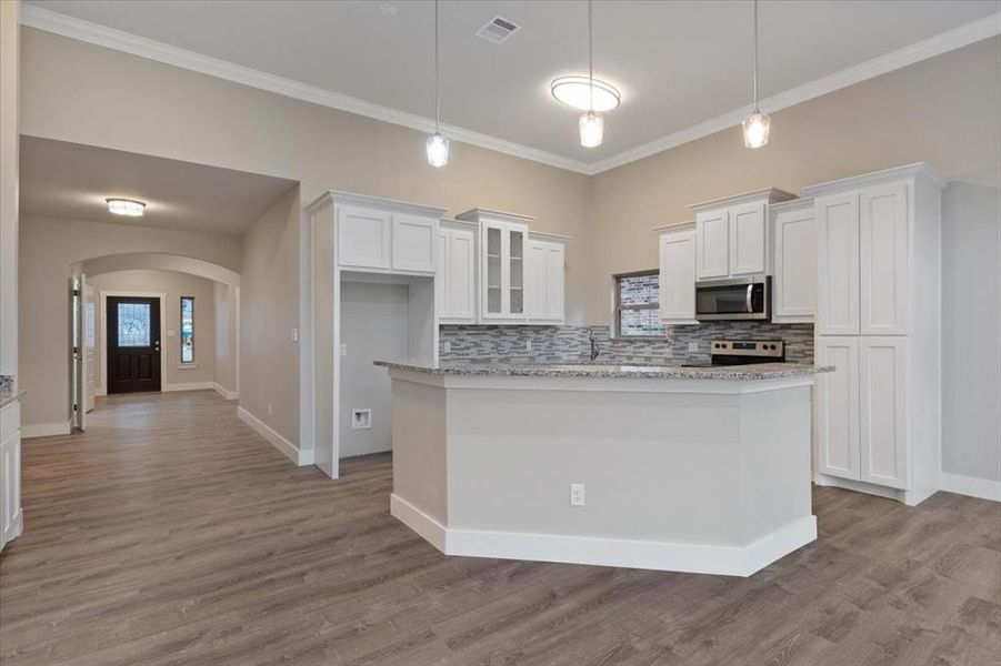 Kitchen featuring tasteful backsplash, stainless steel appliances, hardwood / wood-style floors, hanging light fixtures, and white cabinetry