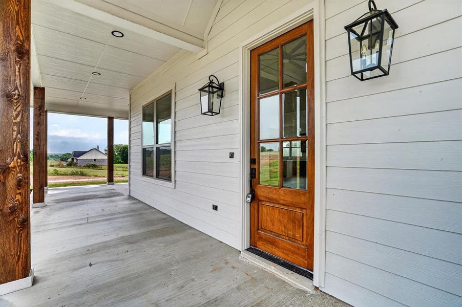 Inviting front porch featuring a wood-panel entry door with glass inserts, white horizontal siding, and rustic wood posts
