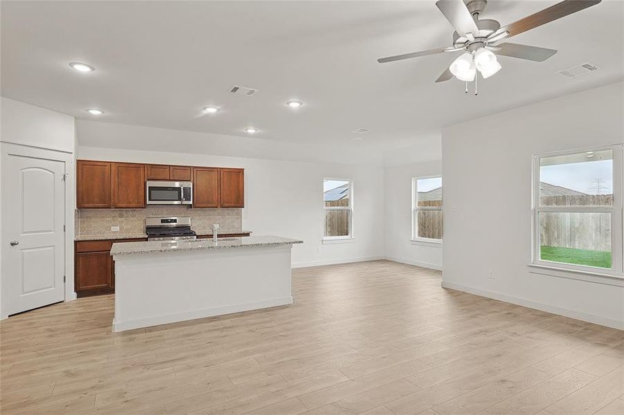 Kitchen with backsplash, appliances with stainless steel finishes, light hardwood / wood-style flooring, and a kitchen island with sink