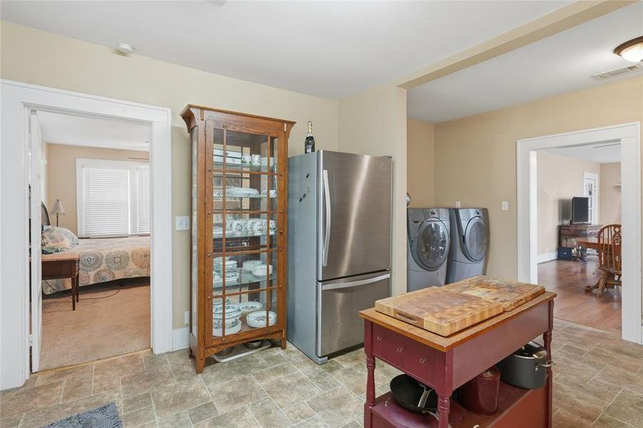 Kitchen area with tile-look flooring, stainless steel refrigerator, and stacked washer and dryer