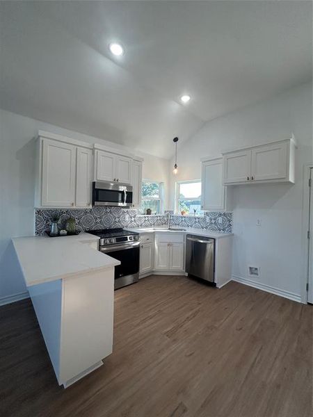 Kitchen featuring white cabinets, stove, lofted ceiling, hanging light fixtures, and dishwasher