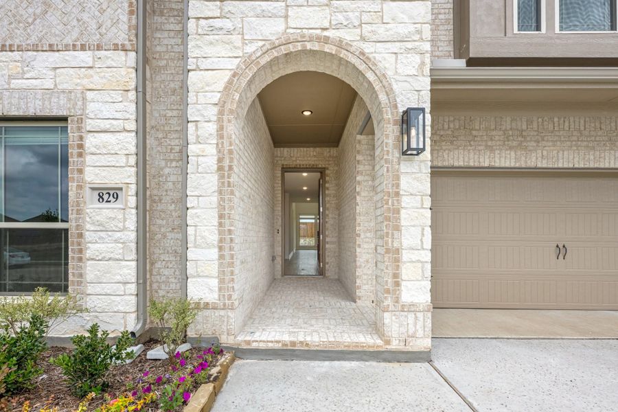 Home entrance with arched stone entryway, covered walkway leading to front door, and attached garage beside it. Home entrance with arched stone entryway, covered walkway leading to front door, and attached garage beside it.