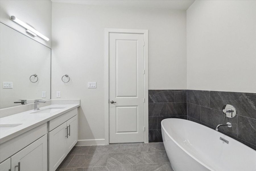 Escape to this luxurious bathroom featuring a deep freestanding soaking tub set against striking dark slate-style tile for a bold, modern look.