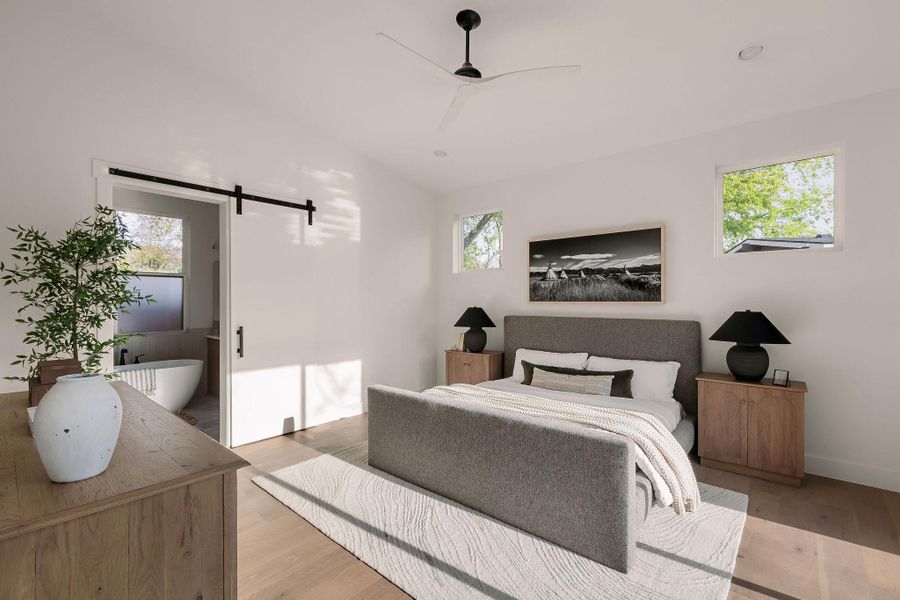 Bedroom with a barn door, light wood-type flooring, multiple windows, and ensuite bath Bedroom with a barn door, light wood-type flooring, multiple windows, and ensuite bath
