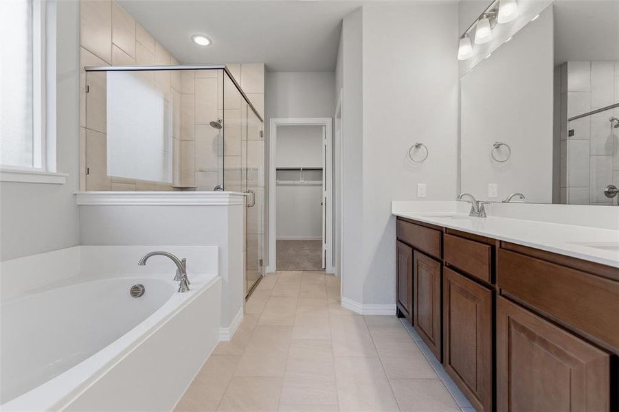Full bath featuring double vanity, a spacious closet, a garden tub, a shower stall, and light tile patterned floors