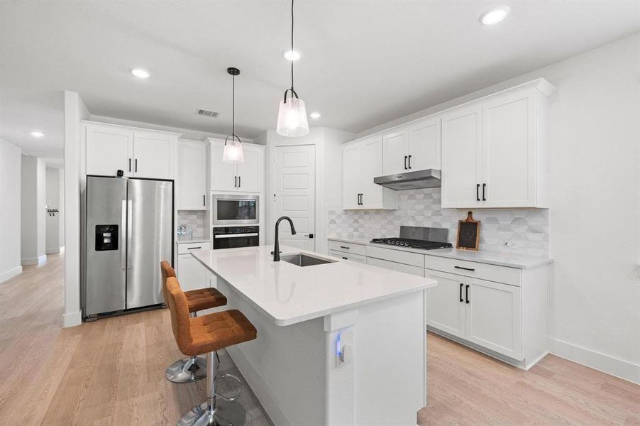 Modern kitchen featuring a central island, white cabinetry with black hardware, stainless steel appliances, and a patterned tile backsplash Modern kitchen featuring a central island, white cabinetry with black hardware, stainless steel appliances, and a patterned tile backsplash